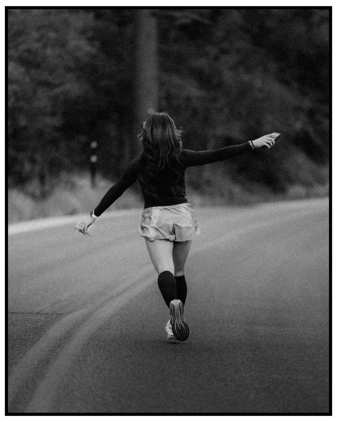 Runner from behind on an open road, arms out, black and white